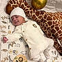 animal_print, baby, balloon, blanket, cozy, cute, decor, infant, knit_hat, knit_onesie, lying_down, milestone, nursery, peaceful, plush_giraffe, sleeping, smiling, soft_toy, striped_socks, wooden_sign