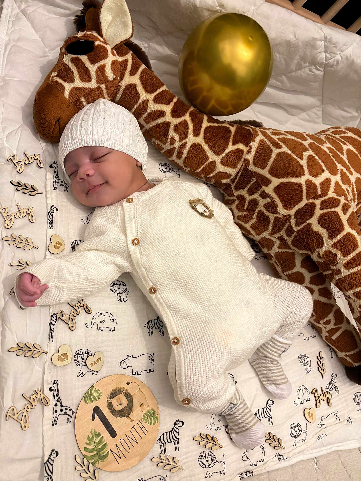 Kazadi a rejoint le concours — aidez-le/la à gagner de superbes lots ! animal_print, baby, balloon, blanket, cozy, cute, decor, infant, knit_hat, knit_onesie, lying_down, milestone, nursery, peaceful, plush_giraffe, sleeping, smiling, soft_toy, striped_socks, wooden_sign