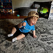 Ryker joined the competition — help win amazing prizes! toddler, child, laughing, blue_shirt, baseball_cap, sitting, rug, indoor, toy_shelf, playpen, wooden_floor, smiling, person, happy, casual_clothing, sock, home, carpet, furniture, playroom