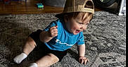 Ryker is registered to the contest to win money with this photo: blue_shirt, cap, carpet, champion, child, face, happy, home, indoor, person, play_area, playpen, rug, shorts, sitting, smiling, toddler, toy_shelf, white_socks, wooden_floor