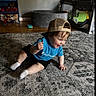 toddler, child, cap, blue_shirt, champion, sitting, rug, indoor, toy_shelf, play_area, smiling, happy, shorts, white_socks, wooden_floor, carpet, face, person, home, playpen