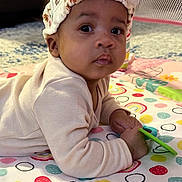 Rayven is registered to the contest to win money with this photo: baby, bow, child, colorful, curious, cute, expression, face, hand, headband, indoors, infant, lying_down, person, play_mat, polka_dots, rainbow, soft_clothing, toy, young