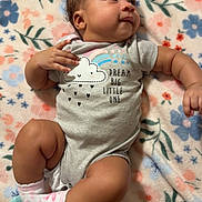 Rayven is registered to the contest to win money with this photo: baby, infant, onesie, socks, blanket, floral_pattern, cute, lying_down, child, soft_texture, smiling, curious, skin, hair, indoors, comfortable, small_hands, small_feet, sleepwear, portrait