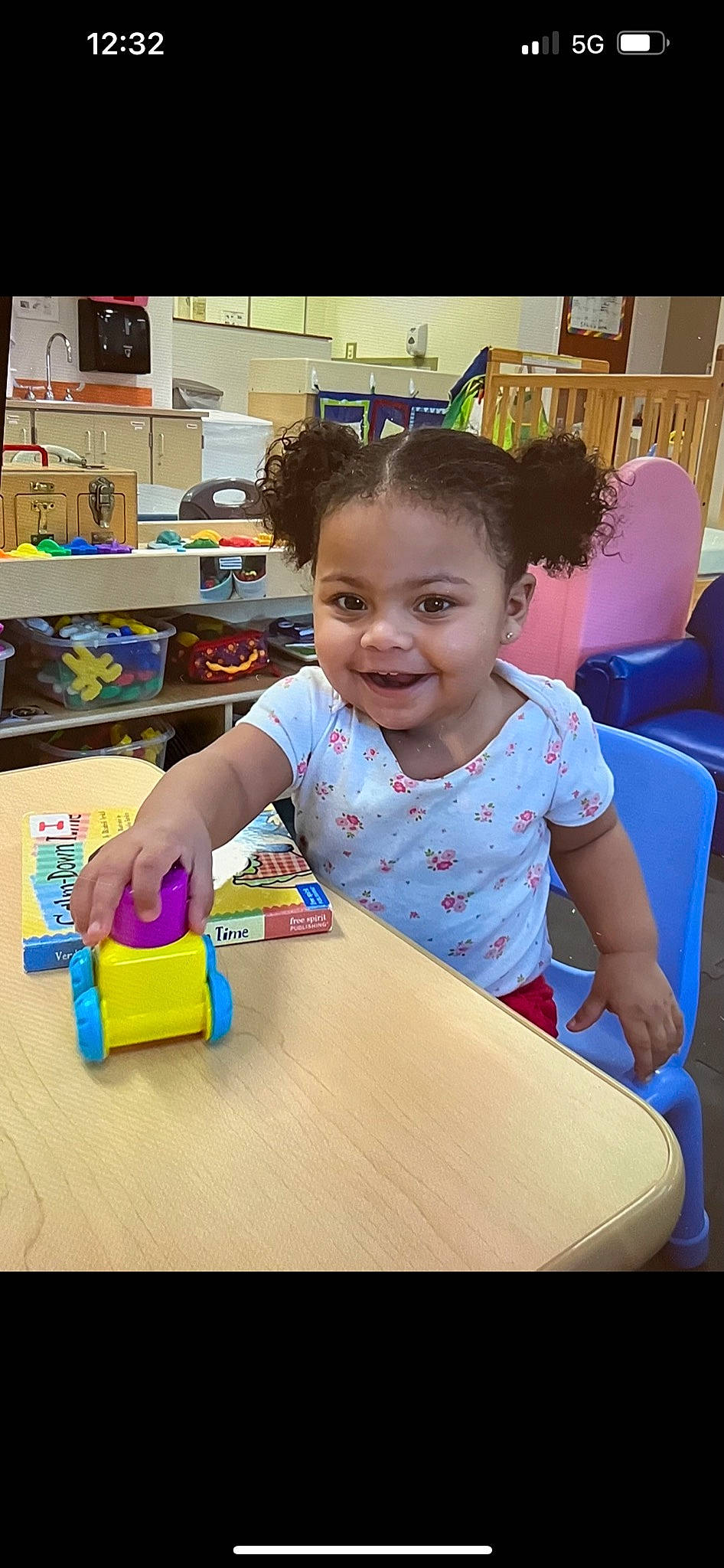 Kianna is registered to the contest to win money with this photo: chair, child, desk, event, finger, fun, happy, joy, kindergarten, leisure, person, recreation, room, sharing, sitting, smile, summer, t_shirt, table, toddler