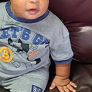 Khylon joined the competition — help win amazing prizes! child, toddler, baby, portrait, sitting, couch, leather_couch, braids, beads, gray_clothing, cartoon_shirt, shorts, shoe, curious, expression, indoor, home, closeup, person, photography