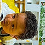 child, curly_hair, face, indoor, yellow_blanket, white_jacket, cozy, portrait, young_child, curious, furniture, wall_art, greenery, modern_room, close_up, skin, expression, head, person, casual