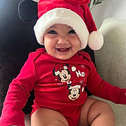 Alba a rejoint le concours — aidez-le/la à gagner de superbes lots ! baby, smiling, red_clothing, santa_hat, mickey_mouse, minnie_mouse, indoor, couch, plant, cute, infant, holiday, christmas, portrait, child, happy, sitting, festive, cozy, person