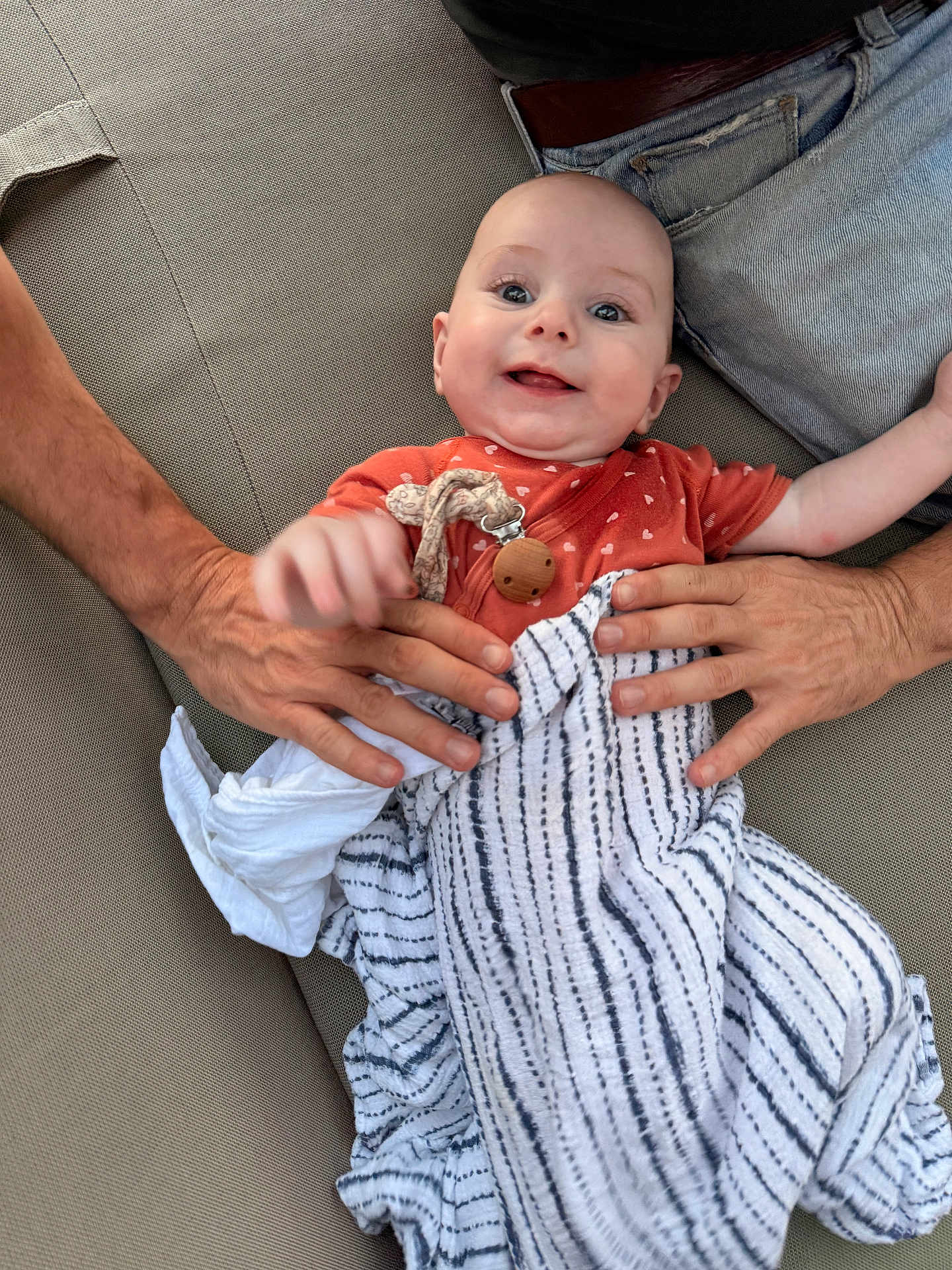 Lola participe au concours pour gagner de l'argent avec cette photo : baby, infant, smiling, adult_hands, blanket, swaddle, pacifier, pacifier_clip, couch, sofa, jeans, belt, face, eyes, portrait, skin, fabric, relaxing, indoor, person