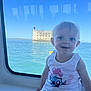 child, toddler, smiling, window, boat, water, sea, fortress, blue_sky, white_tank_top, shorts, blonde_hair, face, happy, sitting, reflection, daylight, cute, portrait, outdoor