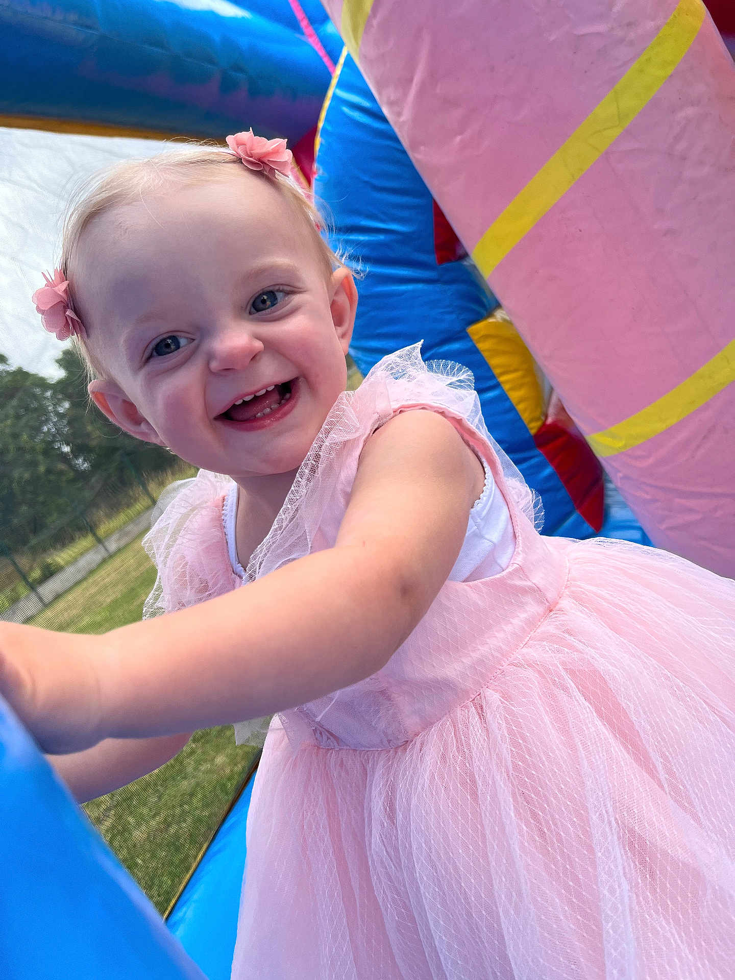 Eliza a rejoint le concours — aidez-le/la à gagner de superbes lots ! toddler, child, smiling, pink_dress, outdoor, inflatable, play, happy, face, hair_accessory, grass, daylight, fun, cute, joy, person, young_child, blue, pink, closeup