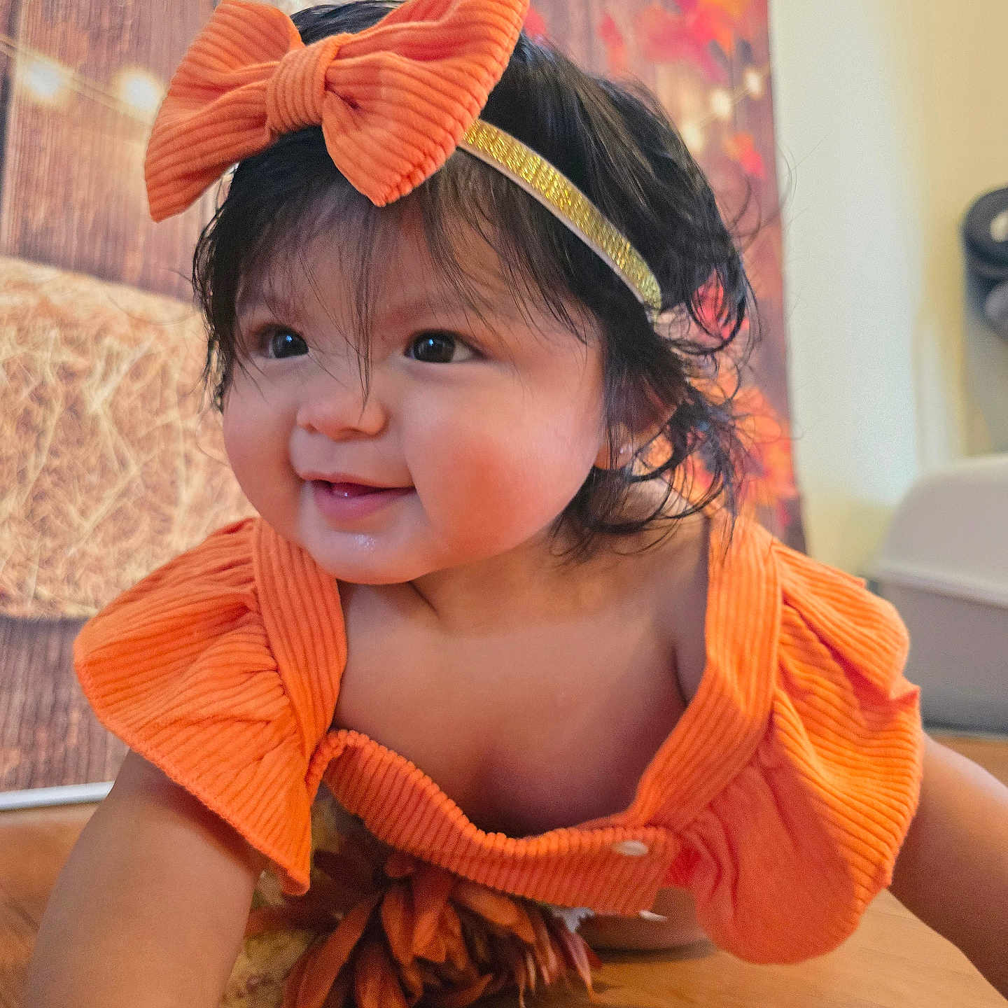 Zoe López is registered to the contest to win money with this photo: autumn, baby, bow, child, closeup, crawling, cute, decor, face, happy, headband, indoor, infant, orange_clothing, person, portrait, smiling, warm_colors, wooden_floor, young_child