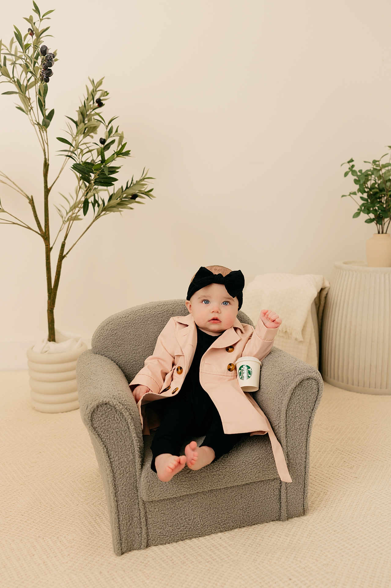 Mallory joined the competition — help win amazing prizes! baby, child, armchair, trench_coat, headband, starbucks_cup, indoor, plant, pottery, minimalist, cozy, carpet, footwearless, cute, portrait, furniture, expression, fashion, relaxing, neutral_colors