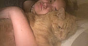 Lenny is registered to the contest to win money with this photo: person, cat, orange_cat, cuddling, indoor, bed, pillow, closeup, face, arm, necklace, resting, cozy, relaxed, fur, pet, animal, sleepy, comfort, warm