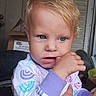 baby, child, toddler, portrait, face, blue_eyes, blond_hair, serious_expression, finger_nibbling, close_up, colorful_clothing, pajamas, indoors, window, adult_hand, supported_child, sitting, photography, home, natural_light