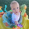 baby, infant, child, portrait, outdoor, grass, activity_center, play_center, baby_toy, colorful, sitting, blue_eyes, blond_hair, pink_clothing, floral_pattern, playful, curious, toy_flower, plastic_toys, daylight