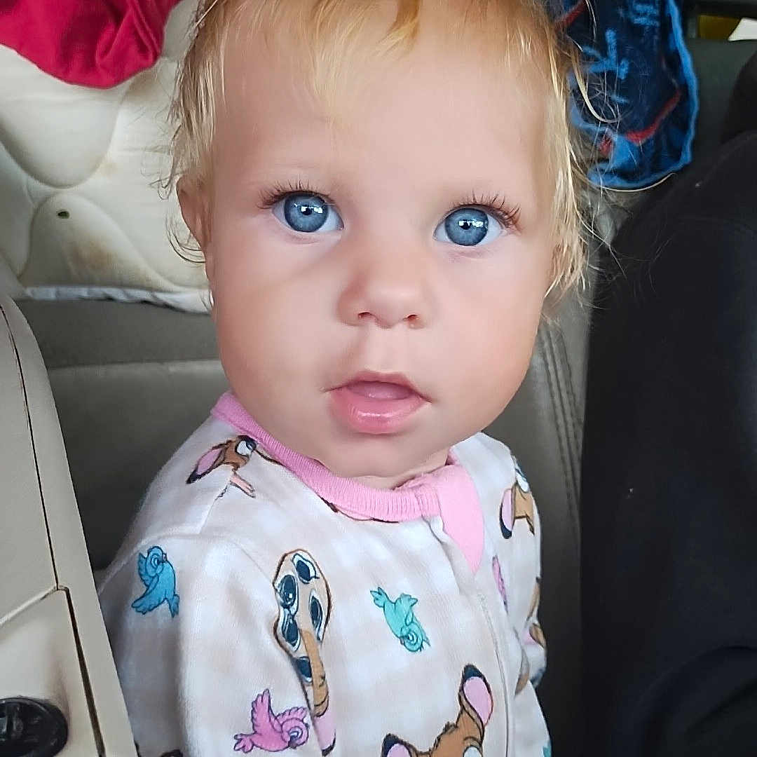 Catherine is registered to the contest to win money with this photo: toddler, child, baby, portrait, car, car_seat, sitting, blue_eyes, blonde_hair, looking_at_camera, facial_expression, pajamas, cartoon_print, clothing, blanket, vehicle_interior, indoors, close_up, daylight, colorful