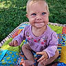 baby, child, sitting, smiling, happy, portrait, outdoor, grass, blanket, patchwork, colorful, purple_clothing, floral_pattern, blue_eyes, blond_hair, infant, hand, barefoot, parked_car, sunlight