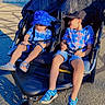 Osman is registered to the contest to win money with this photo: children, toddler, stroller, double_stroller, outdoor, sunlight, summer, siblings, seated, safety_harness, bucket_hat, baseball_cap, plaid_shirt, shorts, sandals, water_bottle, driveway, house, trees, portrait