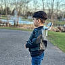 child, boy, profile, outdoors, park, path, jacket, jeans, fashion, portrait, standing, side_view, short_hair, bowl_cut, fountain, trees, chair, nature, daylight, photography