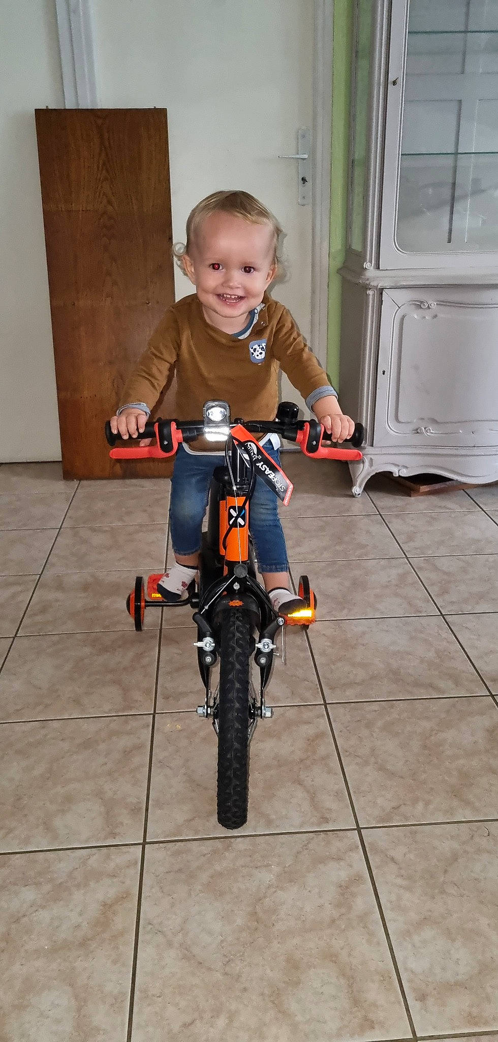Andréas participe au concours pour gagner de l'argent avec cette photo : automotive_tire, bicycle, bicycle_accessory, bicycle_fork, bicycle_frame, bicycle_handlebar, bicycle_part, bicycle_tire, bicycle_wheel, bicycle_wheel_rim, bicycles_equipment_and_supplies, flooring, joy, orange, person, rim, smile, spoke, tire, toddler