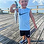 blue_sky, boy, catch, child, clouds, daylight, fish, fishing, happy, nature, ocean, outdoor, person, pier, shorts, sleeveless_shirt, smile, sneakers, summer, wooden_deck