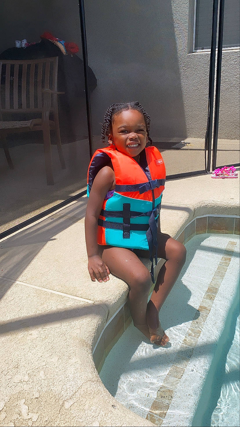 Laylah is registered to the contest to win money with this photo: black_hair, chair, child, electric_blue, foot, fun, happy, human_leg, jewellery, leisure, lifejacket, necklace, person, personal_protective_equipment, recreation, smile, swimwear, thigh, toddler, travel