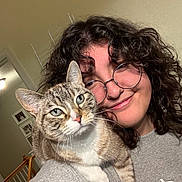 Bella is registered to the contest to win money with this photo: casual_clothing, cat, closeup, cozy, curly_hair, domestic_animal, feline, friendly, glasses, happy, house, indoor, person, photograph, portrait, shoulder, smile, staircase, tabby_cat, wall