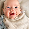 baby, smiling, close_up, face, bib, clothing, infant, portrait, cute, happy, eyes, skin, head, young_child, soft_texture, neutral_background, person, sitting, warm, indoors