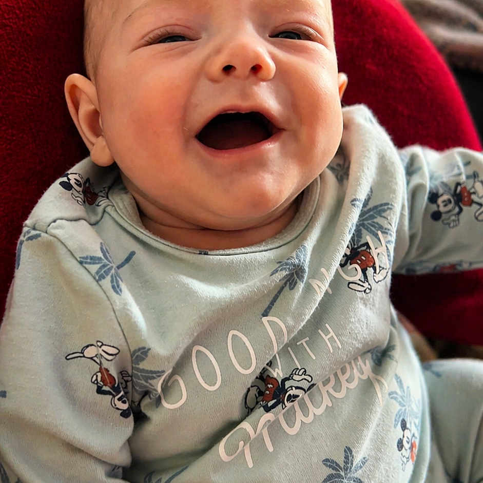 Mylann participe au concours pour gagner de l'argent avec cette photo : baby, smiling, infant, onesie, clothing, red_blanket, remote_control, happy, face, portrait, cute, child, sitting, indoors, person, expression, skin, head, small_child, cozy