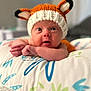 Emberleigh joined the competition — help win amazing prizes! baby, infant, knitted_hat, fox_hat, pillow, patterned_pillow, cute, wide_eyes, lying_down, indoors, soft_lighting, portrait, child, newborn, expression, hand, face, headwear, warm, cozy