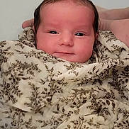 Anna participe au concours pour gagner de l'argent avec cette photo : baby, infant, blanket, wrapped, smiling, face, head, hand, soft_lighting, floral_pattern, cute, newborn, portrait, cozy, warm, skin, expression, young, person, comfort