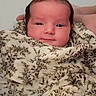 baby, infant, blanket, wrapped, smiling, face, head, hand, soft_lighting, floral_pattern, cute, newborn, portrait, cozy, warm, skin, expression, young, person, comfort