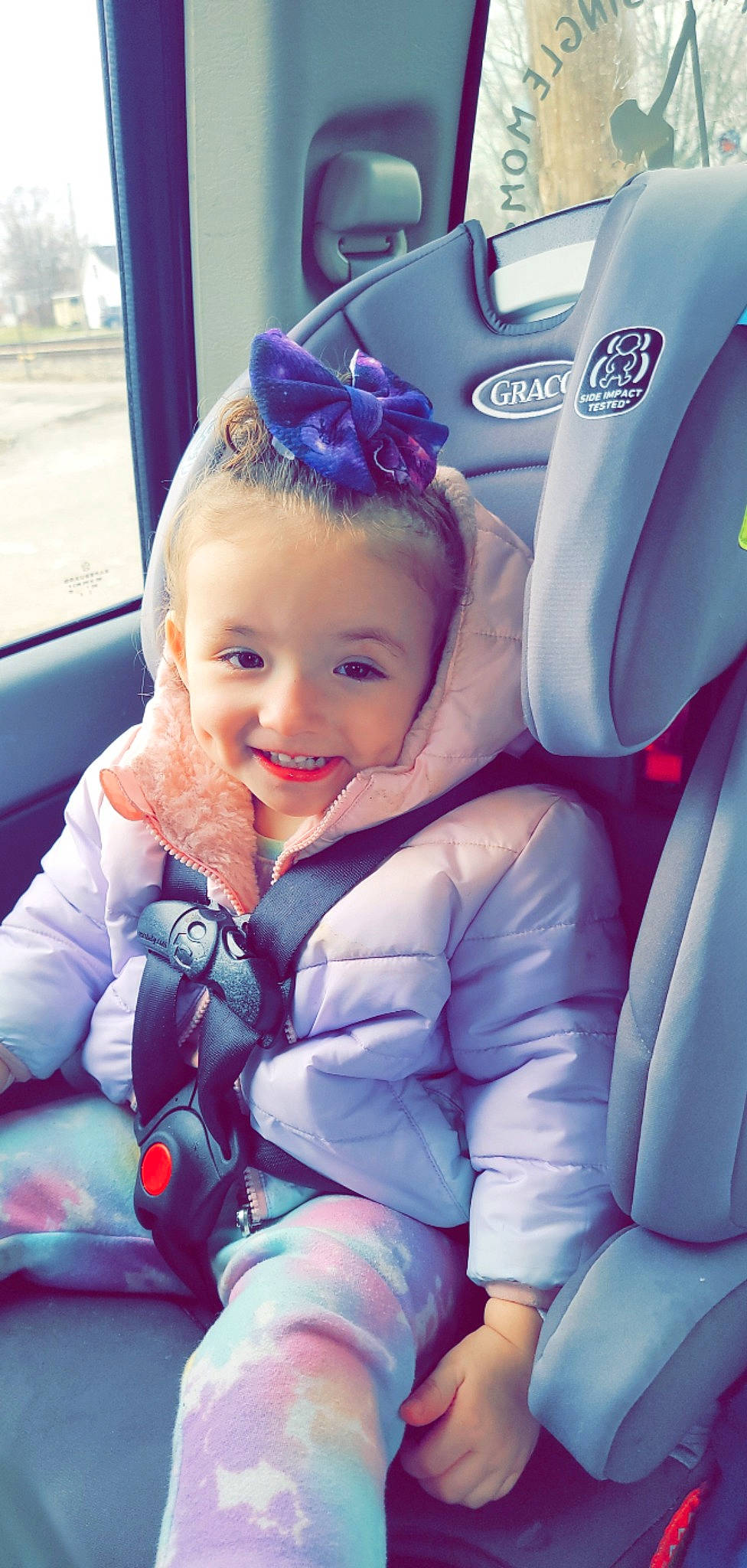 Tara is registered to the contest to win money with this photo: auto_part, automotive_design, baby_toddler_clothing, blue, car, car_seat, car_seat_cover, comfort, electric_blue, facial_expression, finger, happy, joy, person, product, purple, skin, smile, steering_wheel, toddler