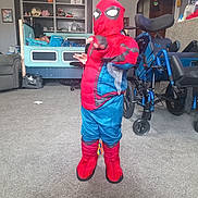 Cohen is registered to the contest to win money with this photo: child, costume, spiderman, indoor, carpet, bed, shelf, toy, wheelchair, furniture, living_room, person, playful, pose, resting, home, decor, boots, mask, carpeted_floor