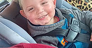 Cohen is registered to the contest to win money with this photo: child, car_seat, smiling, face, seatbelt, leopard_print, bag, clothing, car_interior, window, happy, young, person, safety, seat, head, hair, jacket, casual, indoors