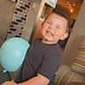 Cohen is registered to the contest to win money with this photo: child, balloon, indoor, smiling, freckles, black_tshirt, happy, living_room, couch, table, can, brick_wall, light, furniture, person, portrait, playful, cute, young, toddler