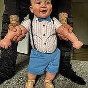 Carter is registered to the contest to win money with this photo: baby, child, smiling, standing, holding_hands, tattoo, blue_shorts, bow_tie, checkered_shirt, sandals, carpet, indoor, person, adult, hands, happy, cute, fashion, floor, support