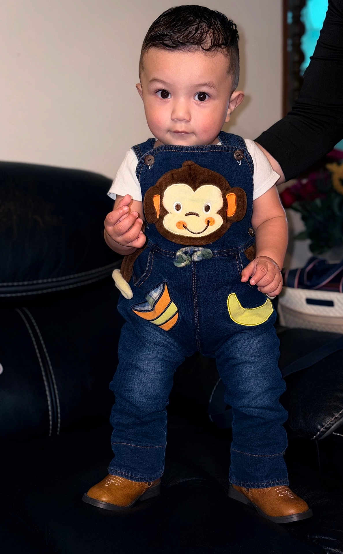 Julian joined the competition — help win amazing prizes! toddler, child, denim_overalls, monkey_patch, boots, leather_couch, indoor, person, cute, smiling, hand, standing, clothing, baby, denim, footwear, portrait, young_child, home, support