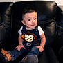 toddler, child, denim_overalls, monkey_patch, boots, leather_couch, smile, curious, indoor, portrait, young_child, fashion, cute, seated, casual_clothing, happy, baby, person, cute_expression, furniture