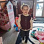 toddler, child, smile, indoor, toy, dollhouse, playroom, wooden_wall, curtain, window, floor_mat, shoes, playing, vest, pants, hair_bow, camera, person, happy, light