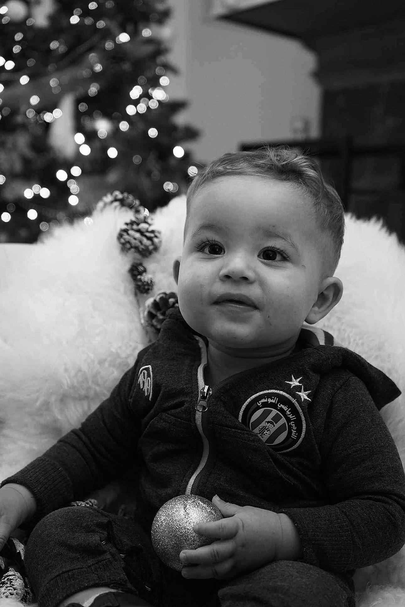 Zakaria a rejoint le concours — aidez-le/la à gagner de superbes lots ! baby, black, black_and_white, cheek, child, christmas_ornament, christmas_tree, eye, facial_expression, flash_photography, hairstyle, happy, head, people, person, photograph, skin, standing, style, toddler