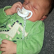 Kalys participe au concours pour gagner de l'argent avec cette photo : baby, sleeping, pacifier, green_clothing, onesie, hand, face, infant, child, resting, cute, soft_texture, indoor, cozy, peaceful, closeup, person, head, young, comfort
