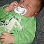 baby, sleeping, pacifier, green_clothing, onesie, hand, face, infant, child, resting, cute, soft_texture, indoor, cozy, peaceful, closeup, person, head, young, comfort