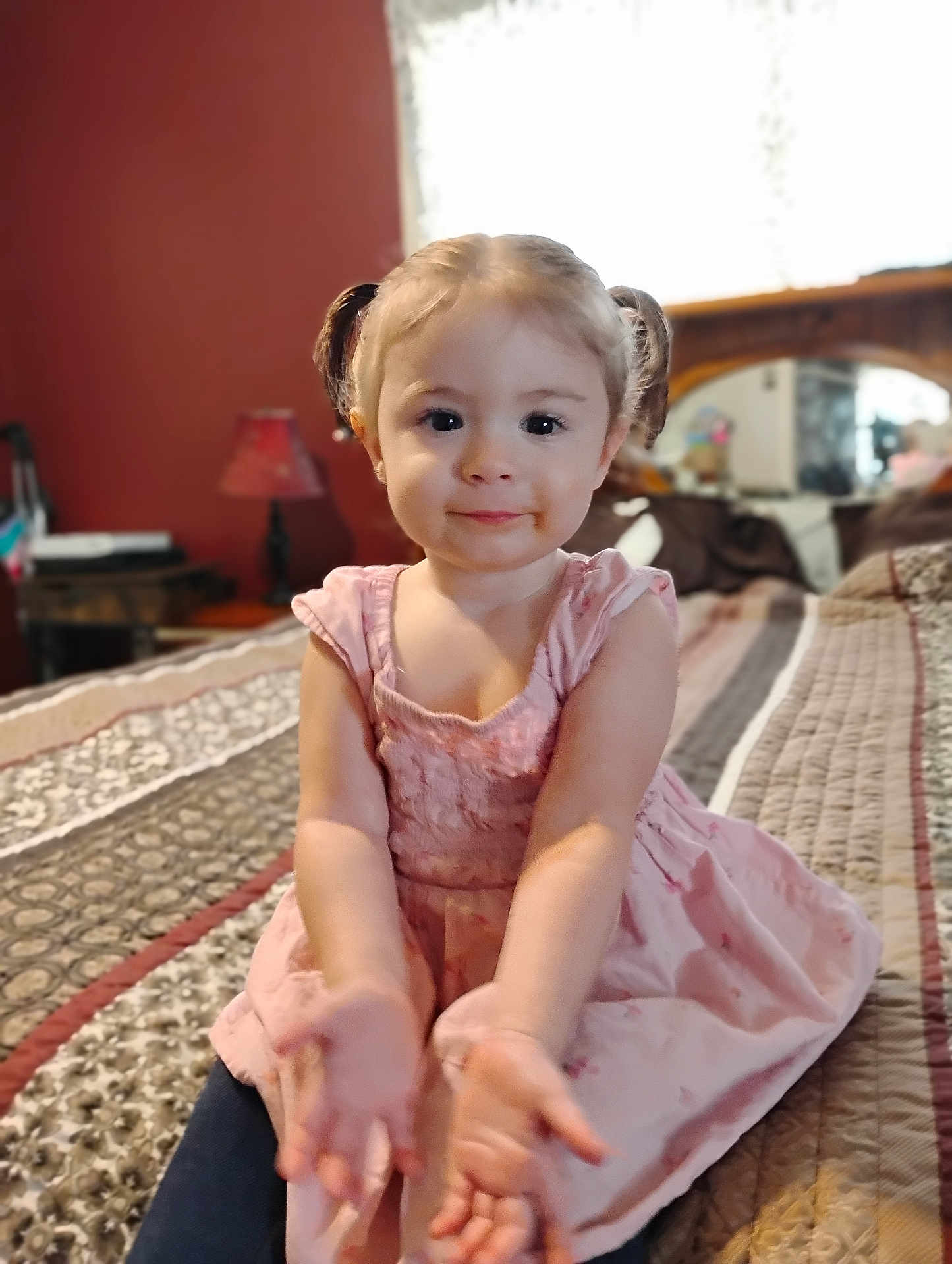 Sarraphena is registered to the contest to win money with this photo: toddler, child, girl, pigtails, pink_dress, bed, bedroom, furniture, lamp, quilt, smiling, portrait, hands, indoor, cute, person, young_child, cozy, home, soft_lighting