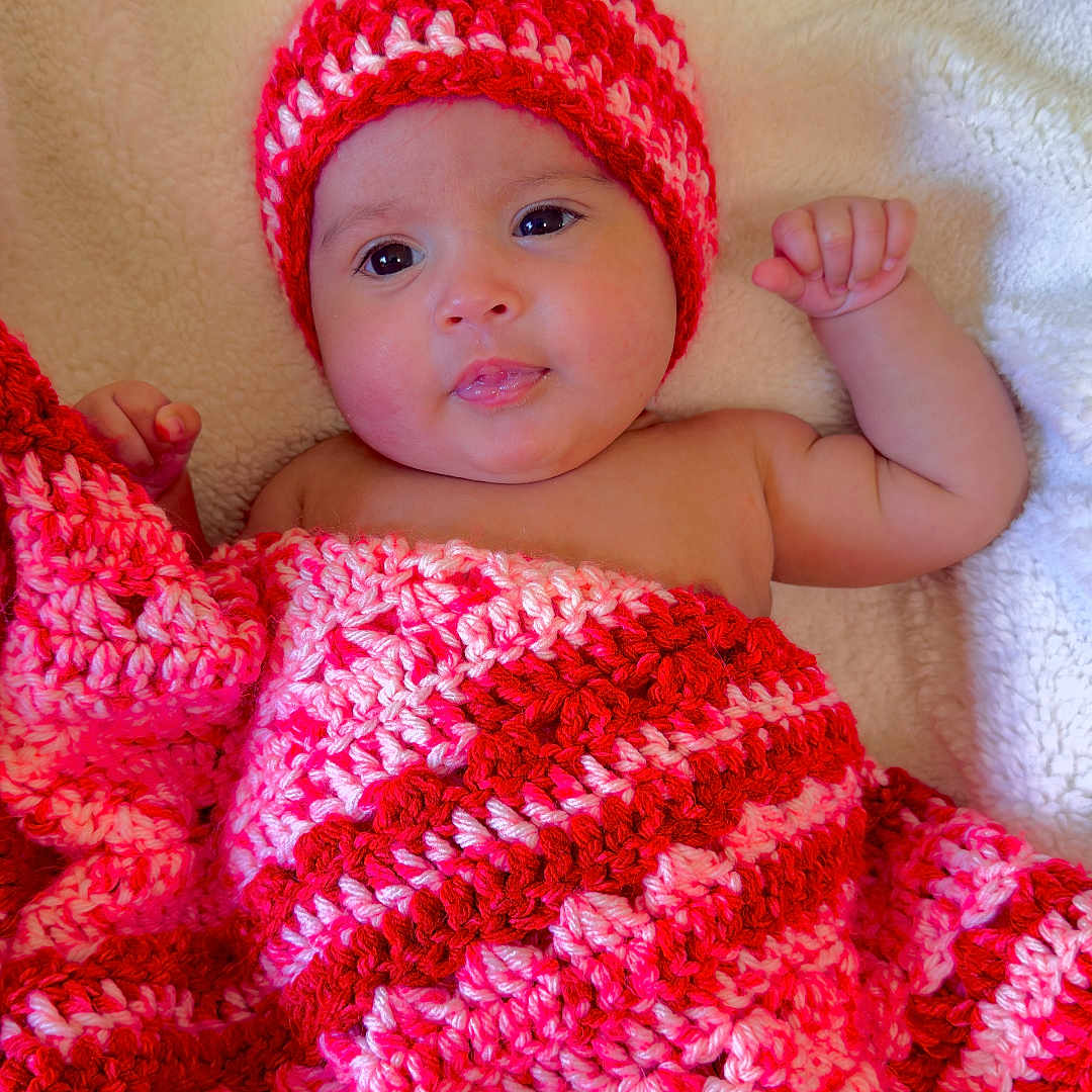 Melody Carballo Paz is registered to the contest to win money with this photo: baby, blanket, child, cozy, crochet, cute, expression, face, hat, indoors, infant, lying_down, newborn, pink, portrait, red, resting, skin, soft, warm
