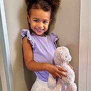 Ciara participe au concours pour gagner de l'argent avec cette photo : child, girl, smile, curly_hair, pigtails, lavender_top, white_skirt, plush_bunny, stuffed_animal, holding_toy, portrait, indoor, happy, cute, young_child, eyes, face, person, wall, fashion