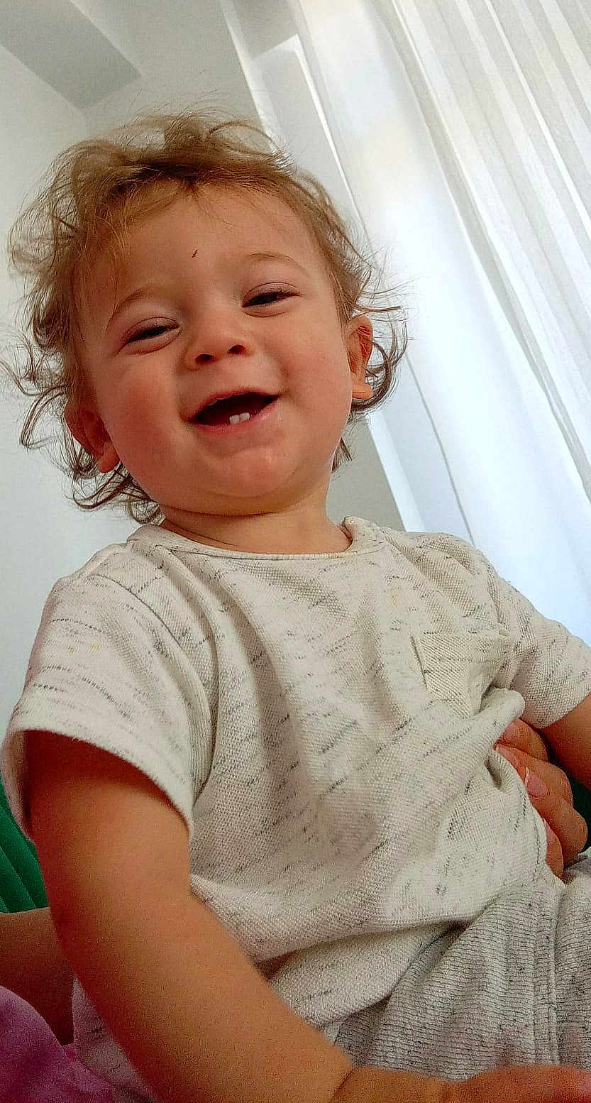 Mehmet participe au concours pour gagner de l'argent avec cette photo : toddler, child, smiling, happy, face, curly_hair, light_clothing, indoor, portrait, baby, cute, person, young_child, natural_light, window, white_curtains, casual_wear, close_up, human, cheerful