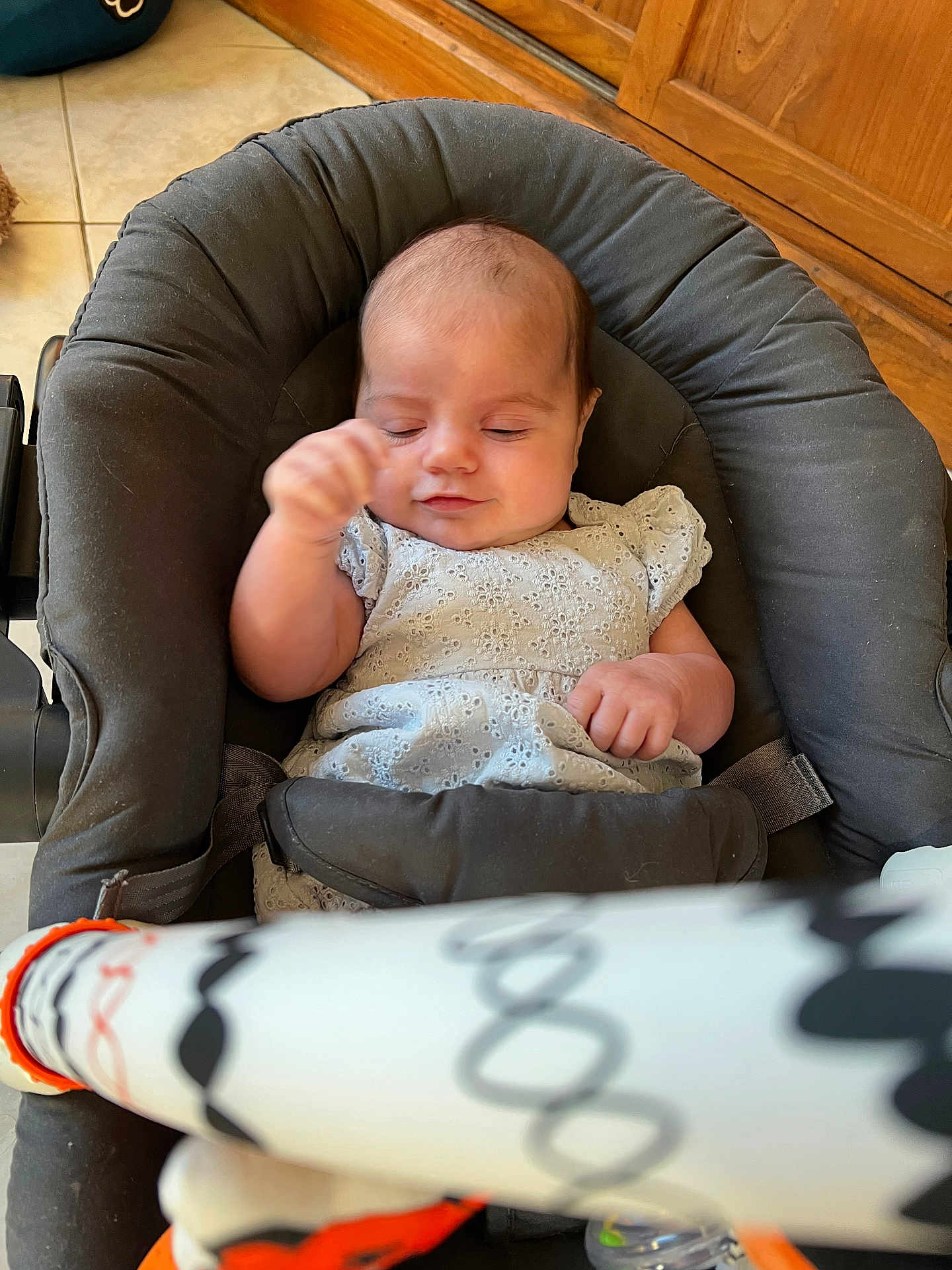 Harleen a rejoint le concours — aidez-le/la à gagner de superbes lots ! baby, infant, baby_seat, white_dress, hand, face, closed_eyes, floor, tile_floor, wood_cabinet, toy_bar, pattern, black_baby_seat, indoor, peaceful, sleepy, child, soft_lighting, portrait, candid
