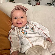 Esmée participe au concours pour gagner de l'argent avec cette photo : baby, child, smile, headband, bow, couch, pillow, plant, indoor, cozy, embroidery, clothing, person, portrait, happy, infant, furniture, relaxing, home, toddler