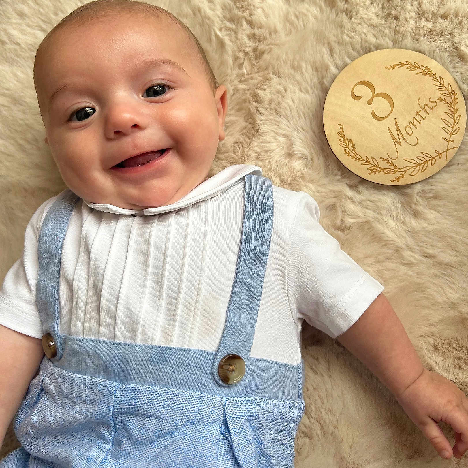 Gabriel participe au concours pour gagner de l'argent avec cette photo : 3_months, baby, blanket, blue_pants, child, clothing, cute, face, fur_texture, hand, happy, infant, lying_down, milestone, portrait, skin, smile, suspenders, white_shirt, wooden_plaque